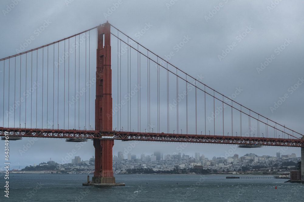 Red metal steel suspension bridge Golden Gate Bridge in San Francisco Bay Area with coast and city downtown skyline silhouette on cloudy day from outdoor cruiseship cruise ship deck Red metal steel suspension bridge Golden Gate Bridge in San Francisco Bay Area with coast and city downtown skyline silhouette on cloudy day from outdoor cruiseship cruise ship deck