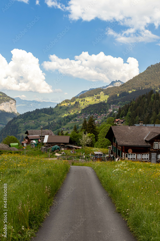 Road Passing By Buildings in the Swiss Alps in Switzerland in the Summer With Mountains Peaking Through the Clouds in the Background