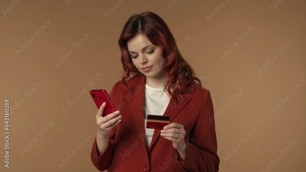 Naklejka premium Medium isolated shot of a joyful, satisfied and relaxed young woman looking at her phone and holding a credit card, completing an online purchase.