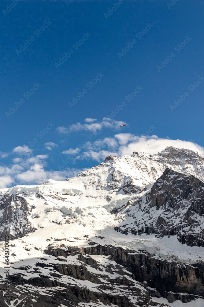 Close Up View of Snow Covered Mountain with Helicopter Flying By in the Swiss Alps in the Summer with Clouds in the Background in Switzerland