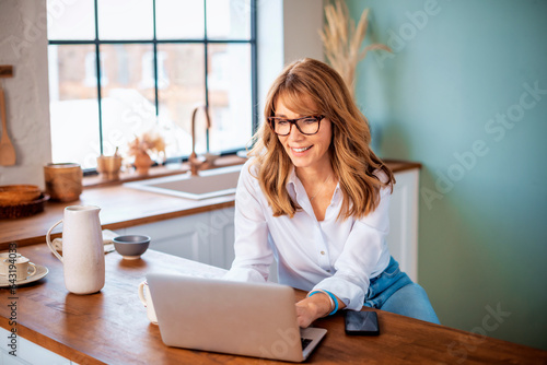 Wallpaper Mural A middle-aged woman standing at the kitchen counter in the morning and using a laptop Torontodigital.ca
