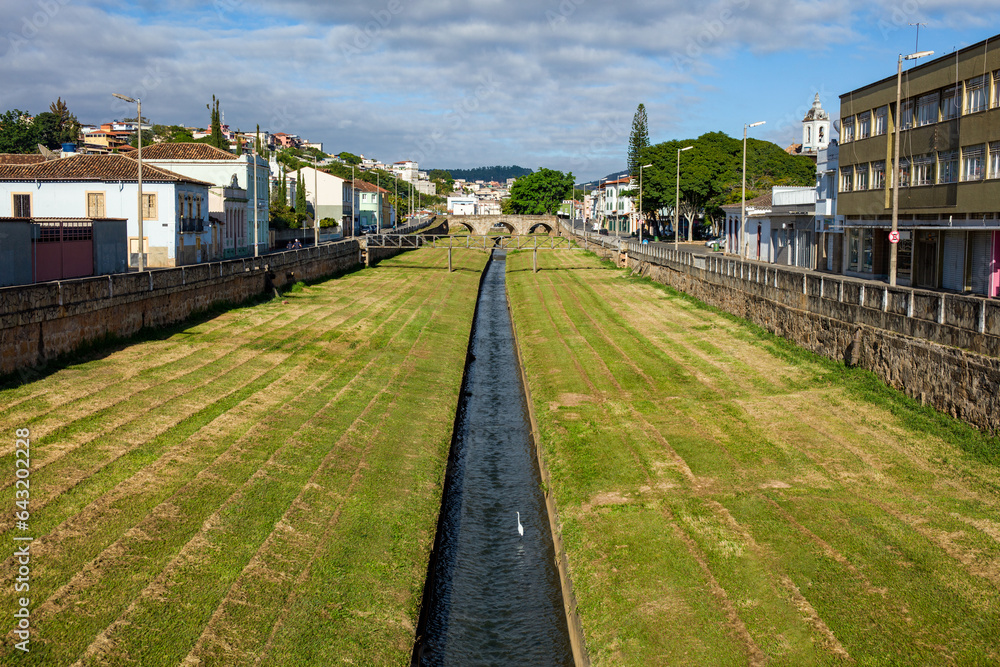 River with green grass and old buildings of the city hall of the historical and tourist city of Sao Joao del Rey, in the state of Minas Gerais, Brazil.