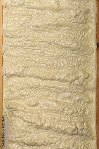 The texture of the construction yellow foam on the wall between the wooden planks.