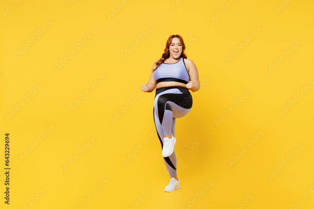 Full body overjoyed excited happy young chubby plus size big fat fit woman wear blue top warm up training do winner gesture isolated on plain yellow background studio home gym. Workout sport concept.