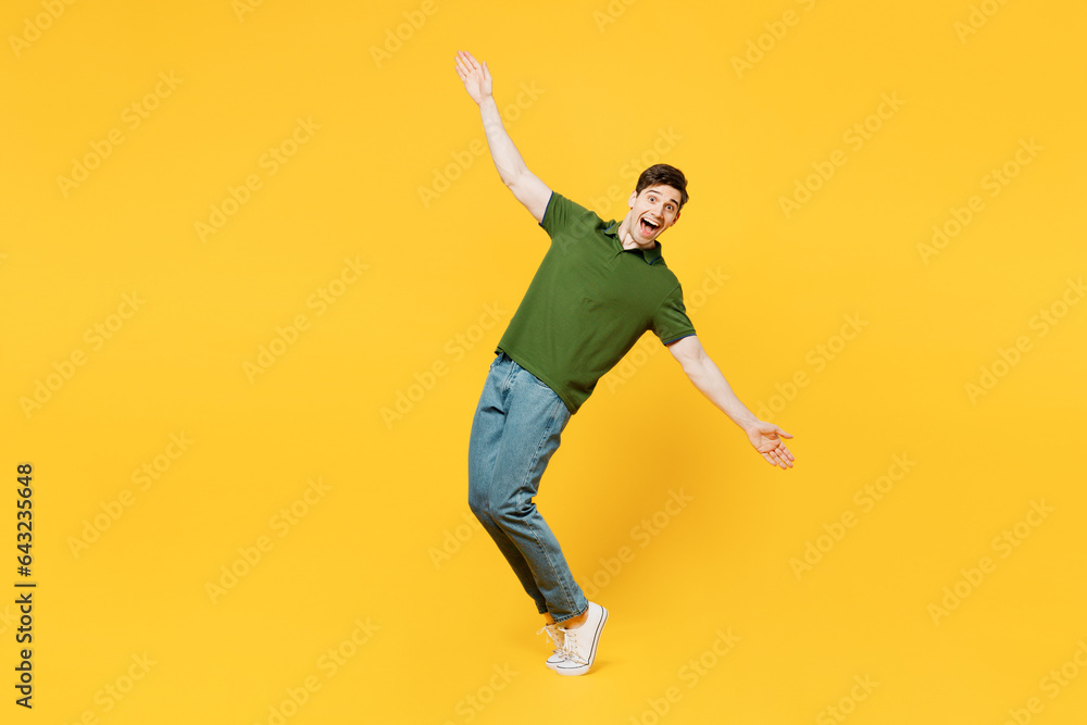 Full body side view young happy man he wearing green t-shirt casual clothes look camera with outstretched hands arms leaning back stand on toes isolated on plain yellow background. Lifestyle concept.