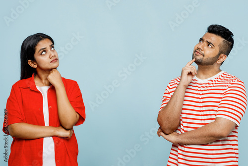 Young minded thoughtful couple two friends family Indian man woman wear red casual clothes t-shirts together look on area between them prop up chin isolated on pastel plain blue cyan color background. photo