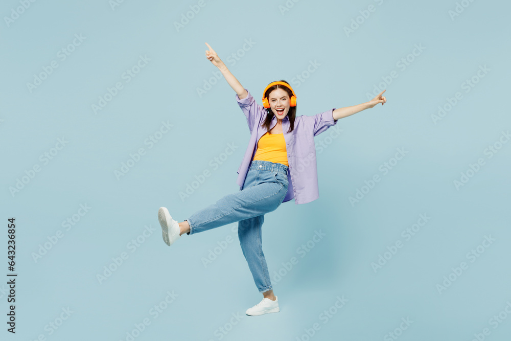 Full body young smiling happy woman she wear purple shirt yellow t-shirt casual clothes listen to music in headphones isolated on plain pastel light blue background studio portrait. Lifestyle concept Full body young smiling happy woman she wear purple shirt yellow t-shirt casual clothes listen to music in headphones isolated on plain pastel light blue background studio portrait. Lifestyle concept