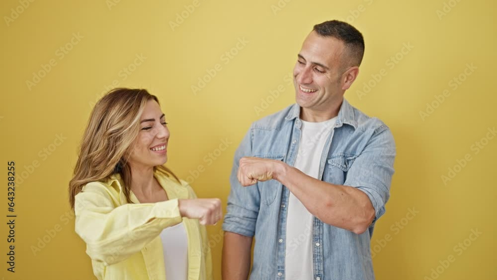 Man and woman couple standing together bump fists over isolated yellow background Man and woman couple standing together bump fists over isolated yellow background