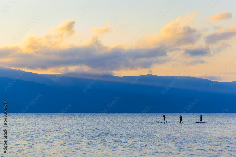 Three stand up paddle boarders silhouetted on calm lake at sunset