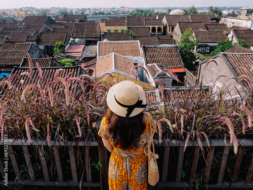 Vietnamese female tourist looks at the ancient rooftops in Hoi An ancient town (Vietnam) from a high-rise cafe photo