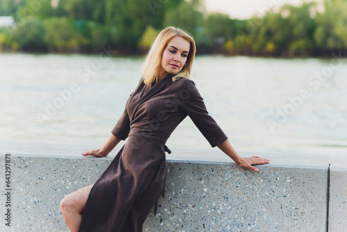 Outdoor portrait of young beautiful caucasuan woman with long straight hair in short black dress, beige shoes holding brown leather handbag walking city street. photo