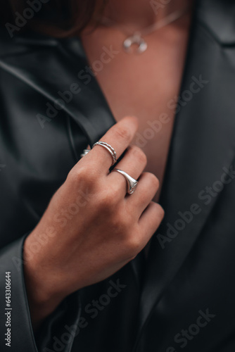Close up fashion details of a black leather jacket and silver ring accessories. Fancy outfit  female accessories