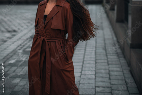 Woman walking alone in the city. Fancy details of autumn long brown leather trench coat. Street style casual clothing