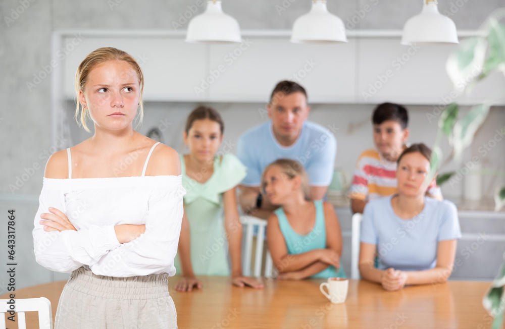 miffed teenager gir with arms crossed over chest standing in front of her big family - obrazy, fototapety, plakaty 