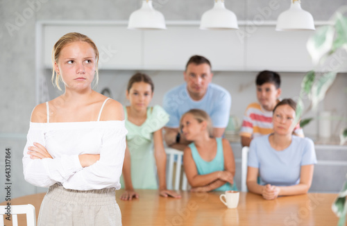 miffed teenager gir with arms crossed over chest standing in front of her big family