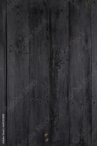 Weathered black wood texture background. Black stained wooden billboard close-up. Vertical direction boards. Wavy pattern of wood fibers.