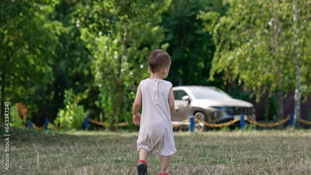 Rear view of a kid in bodysuit walking by the grass. Little toddler spending time outdoors in summer. Rear view of a kid in bodysuit walking by the grass. Little toddler spending time outdoors in summer.