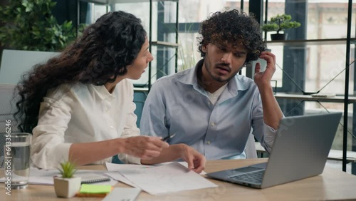 Arabian businesswoman mentor explain financial data teach employee consult trainee help with web project on laptop Indian silly businessman client not understand difficult business learning in office
