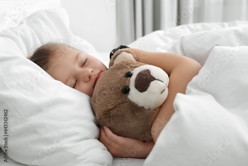 Cute little girl sleeping with teddy bear in bed photo