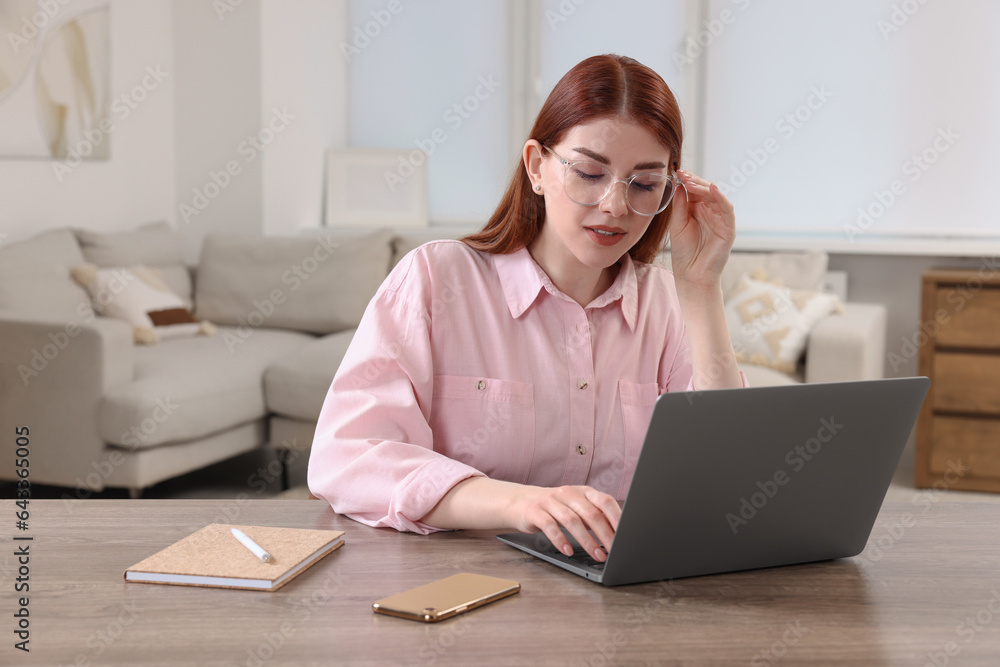 Beautiful woman using laptop at wooden table in room Beautiful woman using laptop at wooden table in room