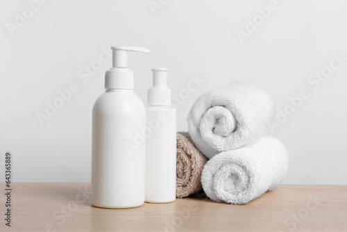 Bottles of cosmetic products and rolled towels on wooden table