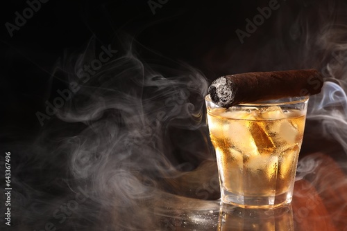 Glass of whiskey with ice cubes and smoldering cigar on black background. Space for text