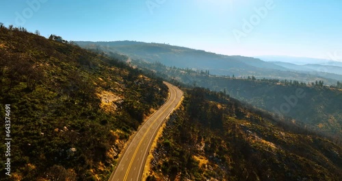 Flying above the sunlit highway in the mountains. Sunny day footage in Sierra National Forest, California, USA.