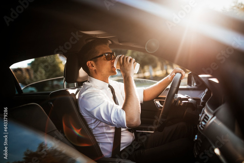 Canvas Print Young caucasian businessman drinking coffee while driving to work