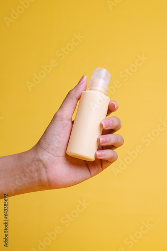 Hand holds bottle for mock up on yellow background. Space for design  concept of skin care.