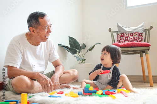 Overjoyed mature grandfather playing with adorable granddaughter at home