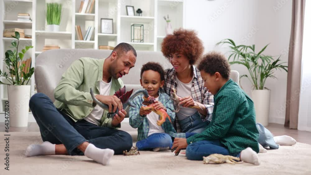 African american family in casual attire playing toys with school-aged sons on floor. Loving father and mother creating happy childhood for children while spending time together in modern apartment African american family in casual attire playing toys with school-aged sons on floor. Loving father and mother creating happy childhood for children while spending time together in modern apartment
