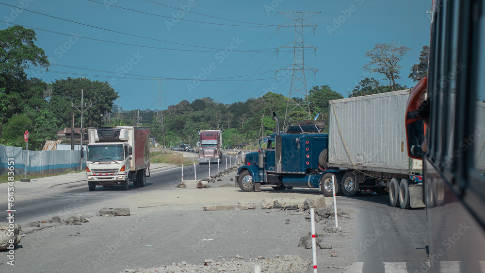 American style truck in blue color turning left and blocking the road behind him. Wide road but still a queue being built behind a truck.