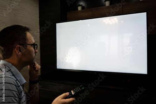 Foto Man watching television, turning on plasma flatscreen TV-set, pointing remote control at empty TV screen