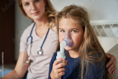 Portrait of elementary age girl  using nebulizer in bed at home