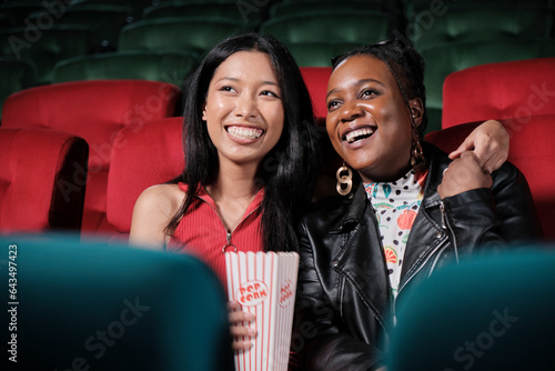 Couple of Black female audiences and lovers express emotion, watching funny cinema together, laughing at movie theater, and entertaining lifestyle with romance film show with happy and cheerful smile.