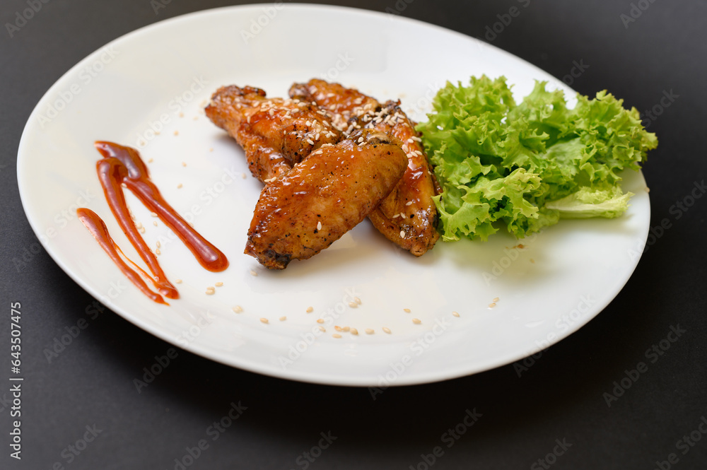 Caramelized chicken wings on a plate with salad and barbecue sauce Caramelized chicken wings on a plate with salad and barbecue sauce