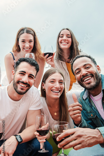 Vertical portrait of a group of young adult multiracial 30s friends having fun on a winery with wine glasses taking a selfie together. Men and women enjoying their friendship on party celebration fest