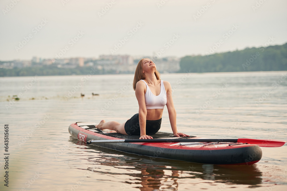 Forest and houses on background. Young woman is on sup boards in the lake