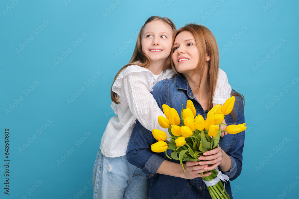 Mother and her cute daughter with bouquet of yellow tulips on light blue background. Space for text Mother and her cute daughter with bouquet of yellow tulips on light blue background. Space for text