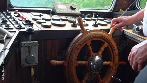 Hands turning old fashioned wooden helmsman wheel on a boat - Handheld closeup of Wheel inside wheelhouse photo