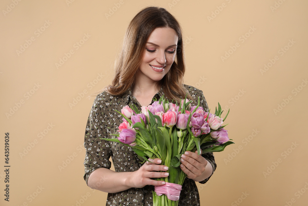 Happy young woman holding bouquet of beautiful tulips on beige background Happy young woman holding bouquet of beautiful tulips on beige background