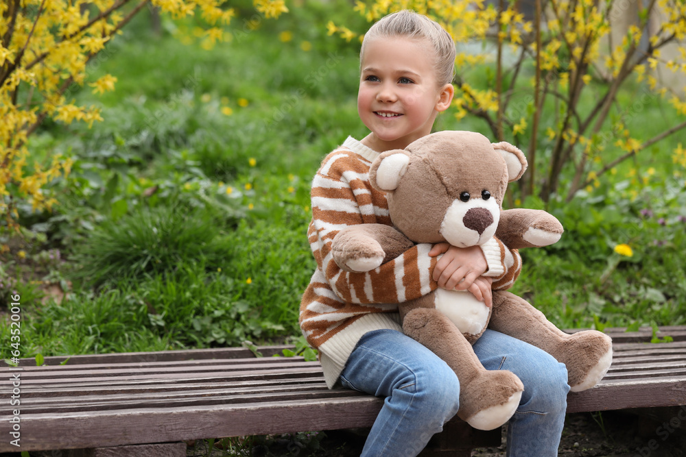 Little girl with teddy bear on wooden bench outdoors. Space for text Little girl with teddy bear on wooden bench outdoors. Space for text