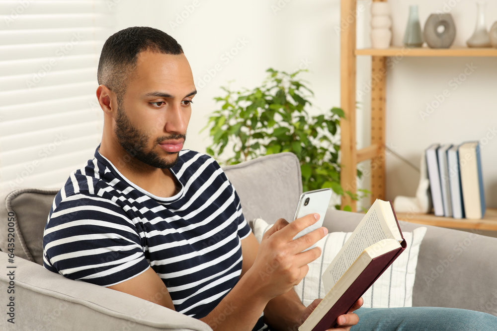 Young man using smartphone while reading book at home. Internet addiction Young man using smartphone while reading book at home. Internet addiction