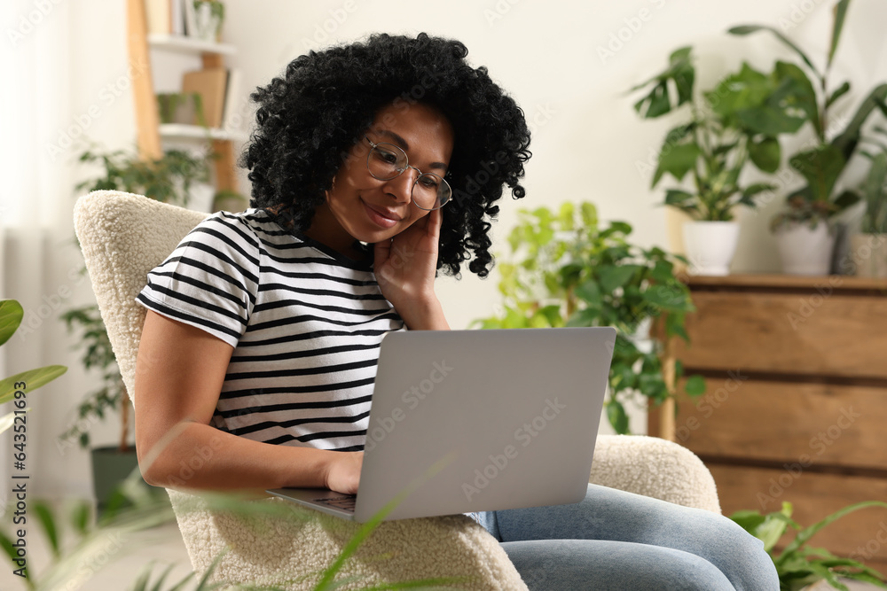 Relaxing atmosphere. Woman with laptop sitting in armchair surrounded by houseplants at home Relaxing atmosphere. Woman with laptop sitting in armchair surrounded by houseplants at home