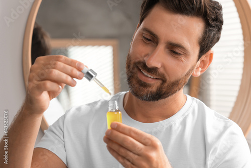 Smiling man with bottle of cosmetic serum indoors