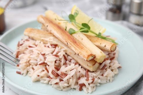 Plate with baked salsify roots, lemon and rice on table, closeup photo