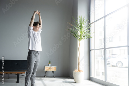 Full body of man stretching and elongating by the window in the morning sun photo