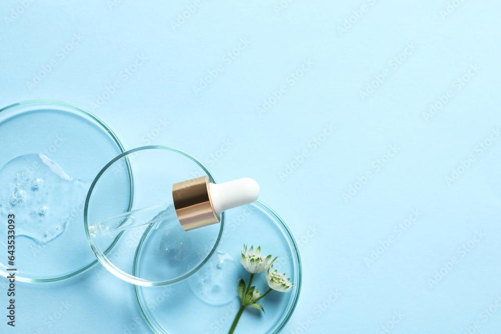Petri dishes with samples of cosmetic oil, pipette and beautiful flowers on light blue background, flat lay. Space for text