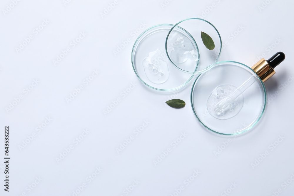 Petri dishes with samples of cosmetic oil, pipette and green leaves on white background, flat lay. Space for text Petri dishes with samples of cosmetic oil, pipette and green leaves on white background, flat lay. Space for text