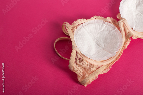 Women\'s bra with liners against the flow of milk from the breast of a nursing woman on a pink background. Copy space for text